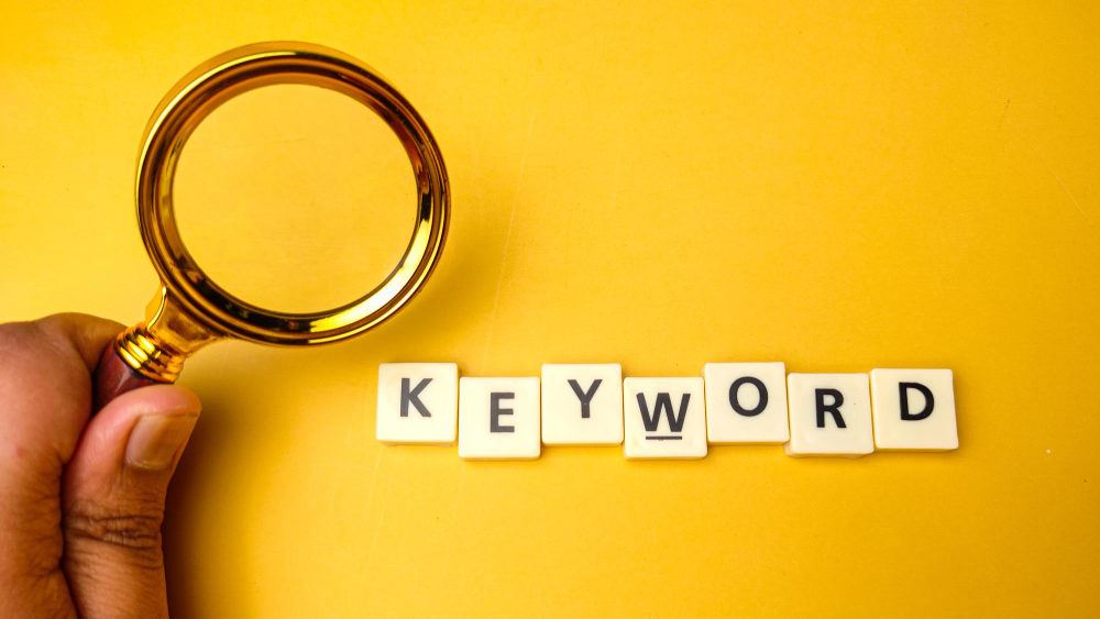 the word "keyword" for keyword research with a gold magnifying glass and yellow background